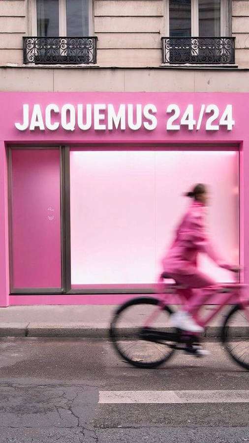 A cyclist in pink passes a pink Jacquemus store on a city street. — Jacquemus Wallpaper