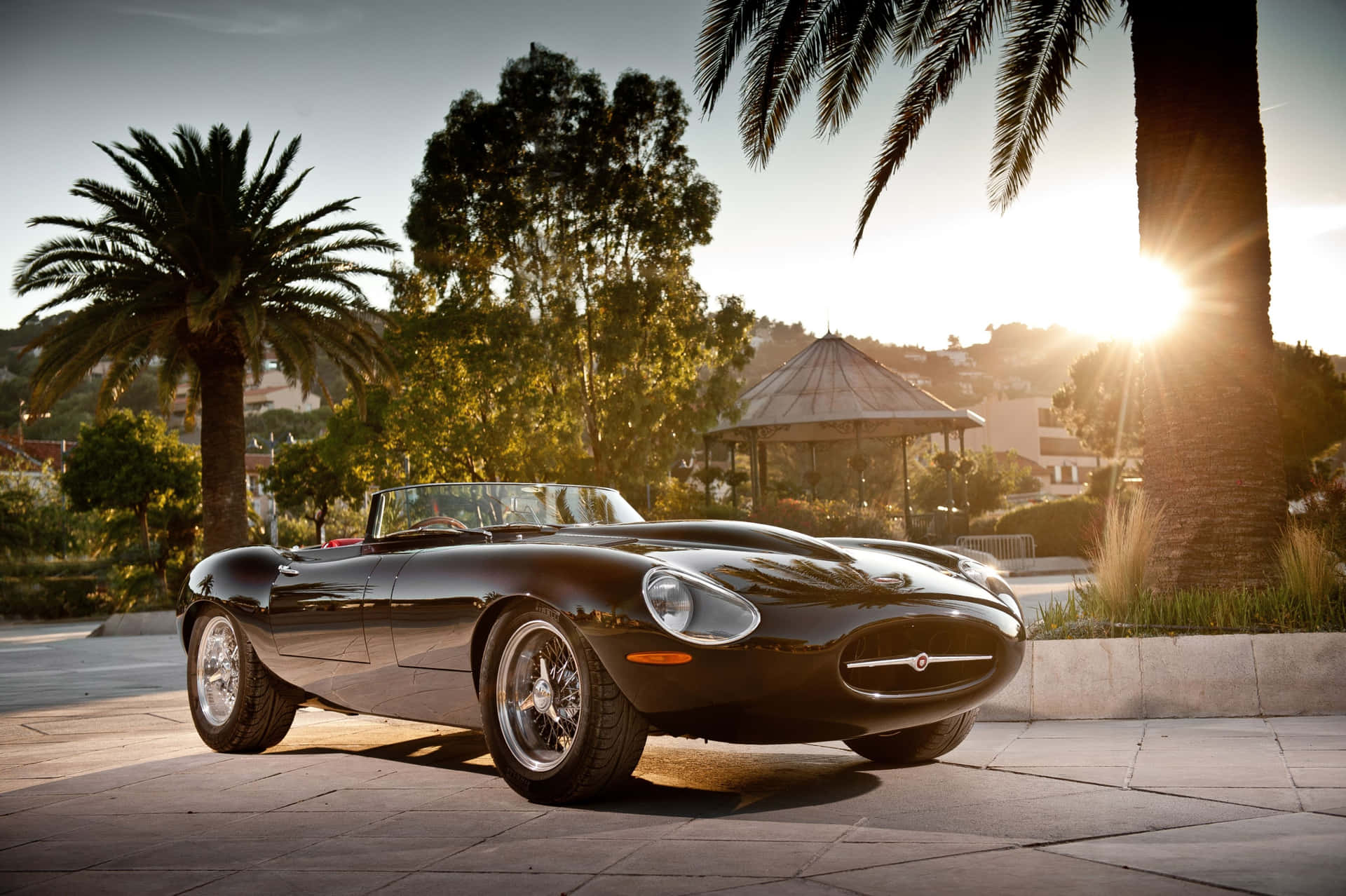 Decappottabile classica nera parcheggiata su patio in pietra con palme e bagliore del tramonto. — Jaguar E-type Sfondi