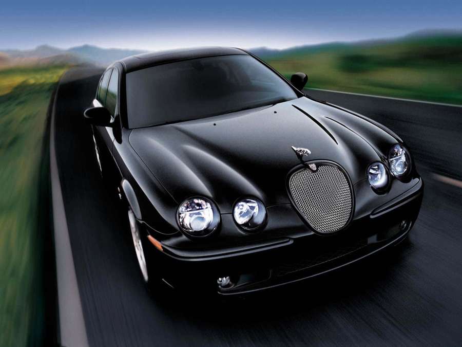Black luxury car speeding on a winding road through green hills. — Jaguar S-type Wallpaper