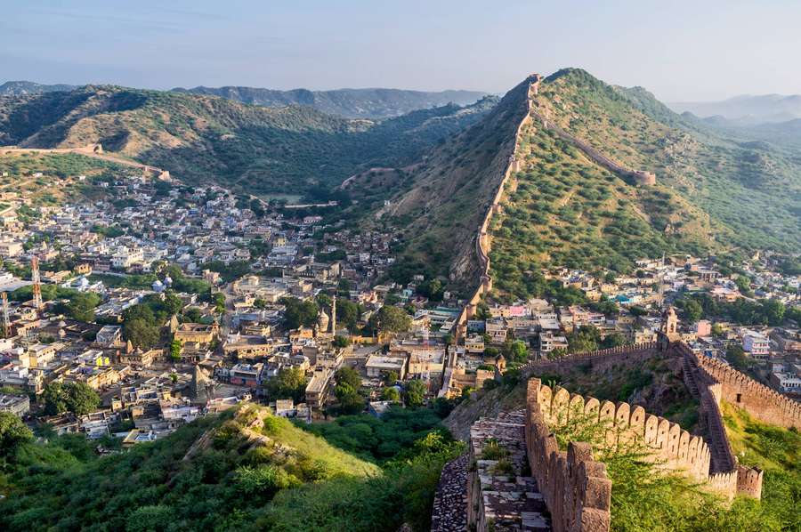 Ancient fort walls climb a green hill overlooking a dense historic town. — Jaipur Background