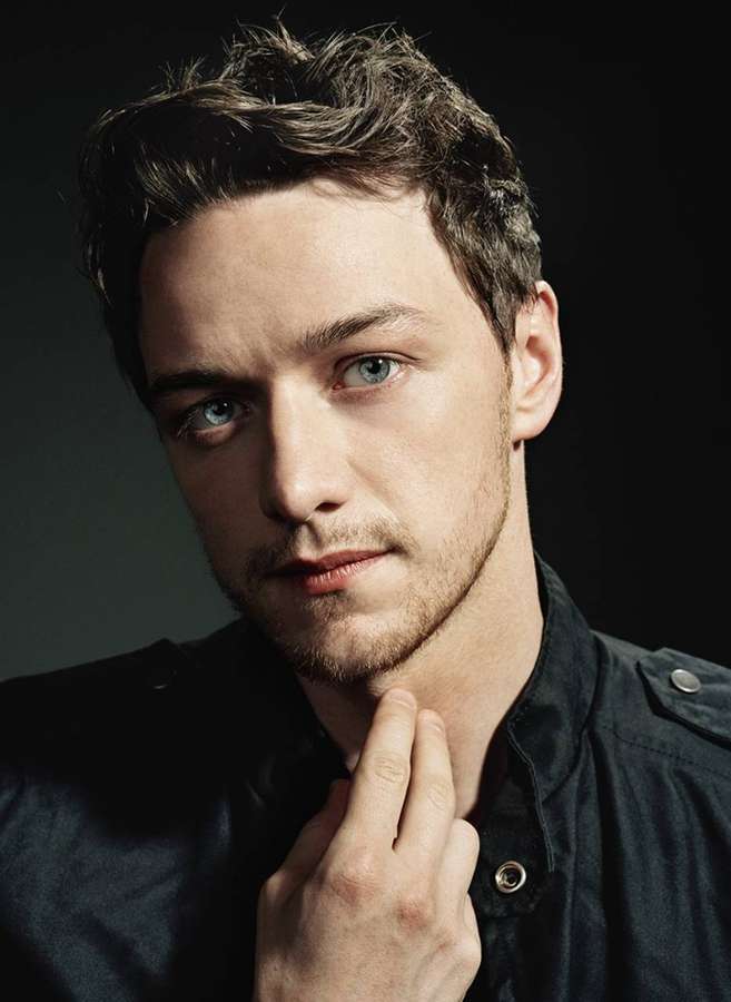 A man with blue eyes and dark hair touching his neck in a studio portrait. — James mcavoy Wallpaper