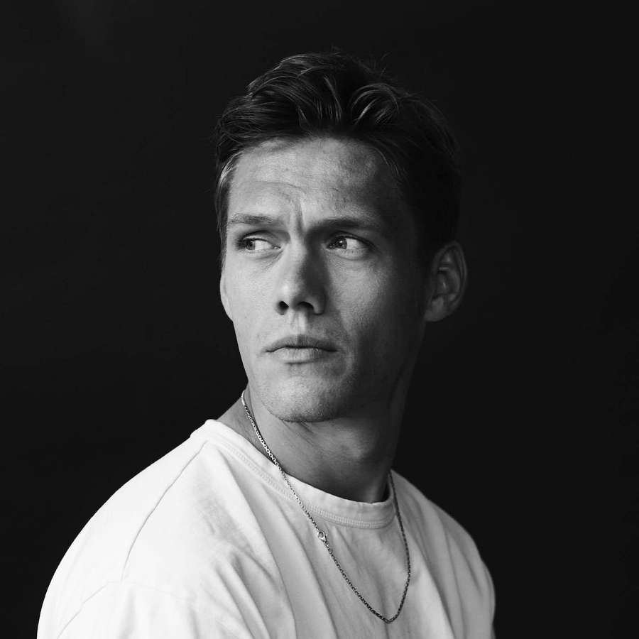 A man in a white t-shirt and chain necklace looking away in a studio portrait. — Jannik Vestergaard Wallpaper