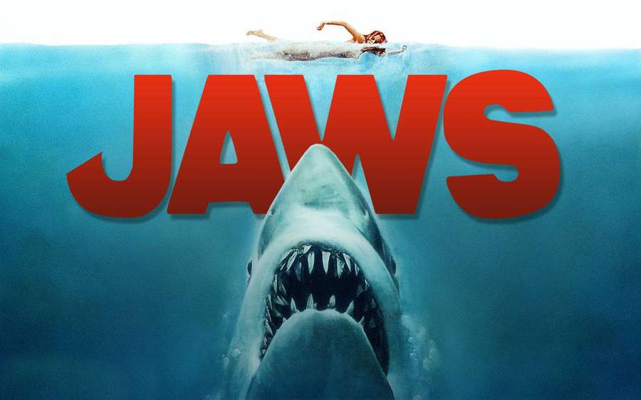 A swimmer floats above water as a shark rises from below with the word JAWS in red. — Jaws Background