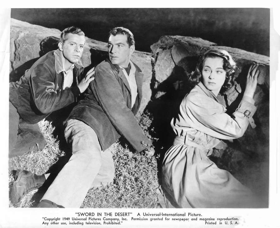 Three actors crouching behind rocks in a tense desert scene from a 1940s film. — Jeff Chandler Background