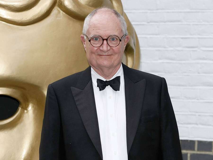 Man in tuxedo standing before golden BAFTA statue — Jim Broadbent Wallpaper