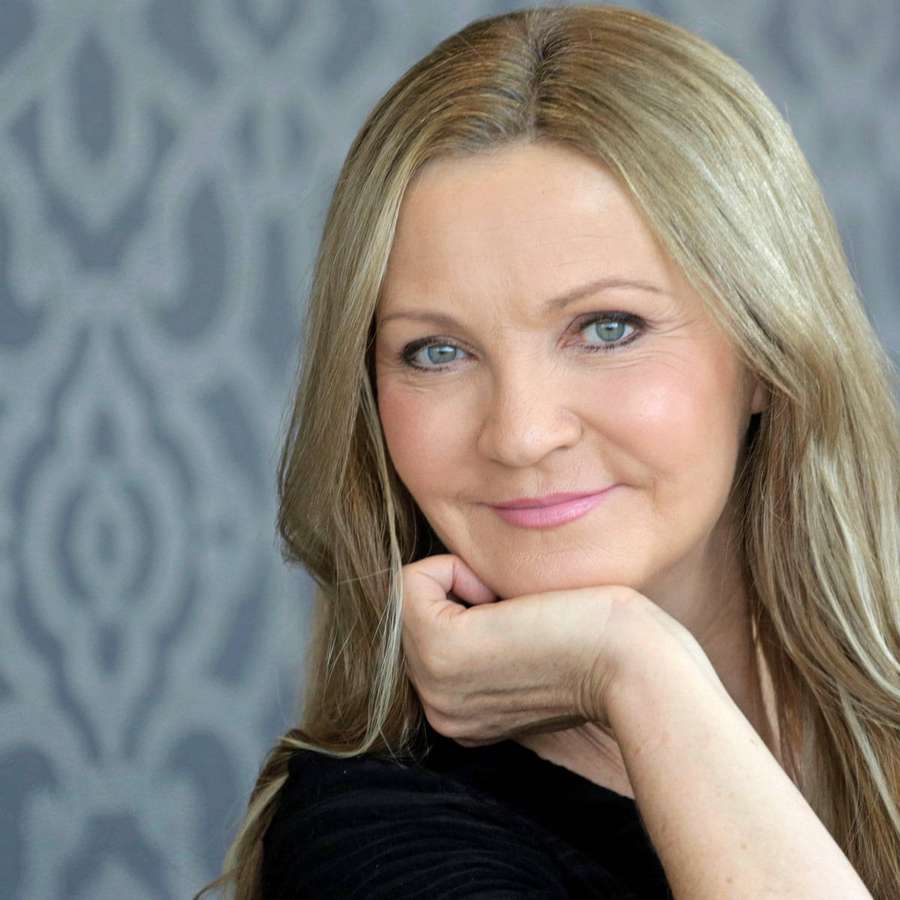 En kvinde med blond hår og blå øjne smiler, mens hun hviler hagen på hånden. — Joan Allen Wallpapers
