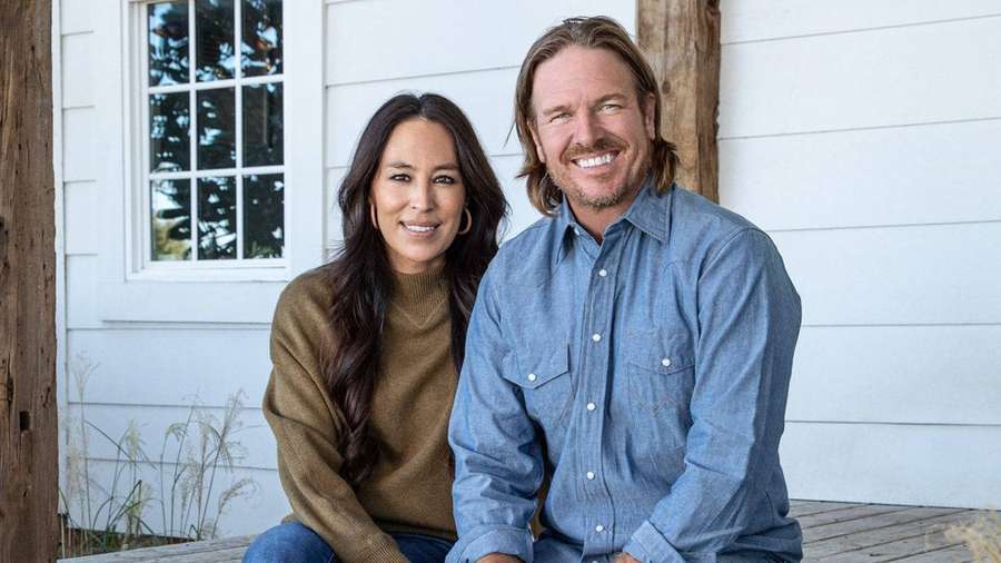 A happy couple sitting on a porch in front of a white house. — Joanna Wallpaper