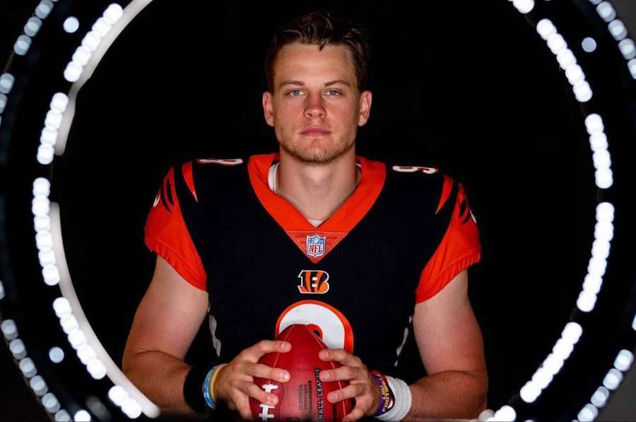 Football player in Bengals uniform holding a football inside a circular light ring. — Joe Burrow Wallpaper