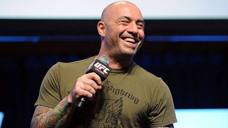 Uomo calvo con tatuaggi ride mentre tiene un microfono UFC sul palco. — Joe Rogan Sfondi