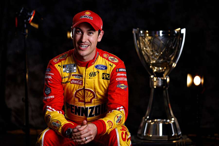Rennfahrer in Rennanzug neben Meisterschaftstrophäe im Studio. — Joey Logano Wallpaper