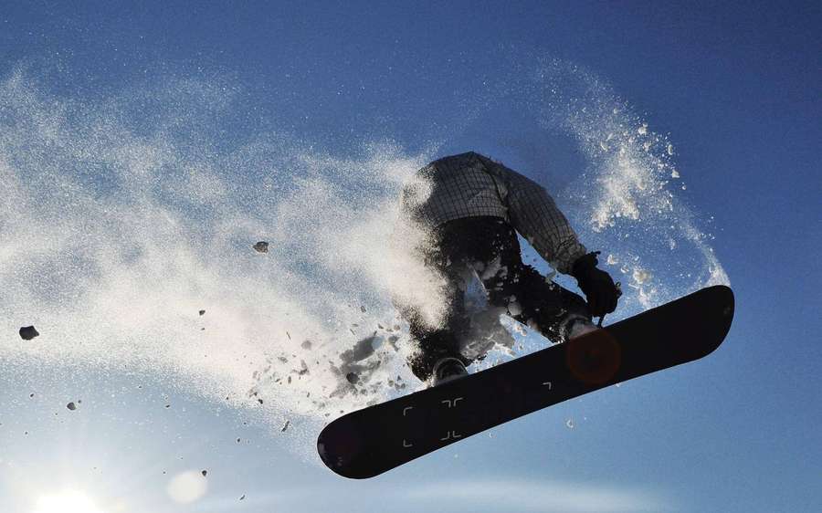 Snowboarder no ar espirrando neve contra céu azul — Jogos X Papéis de Parede