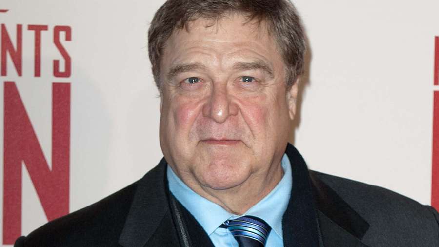 Hombre con traje y corbata en evento con fondo de letras rojas. — John Goodman Fondos de pantalla