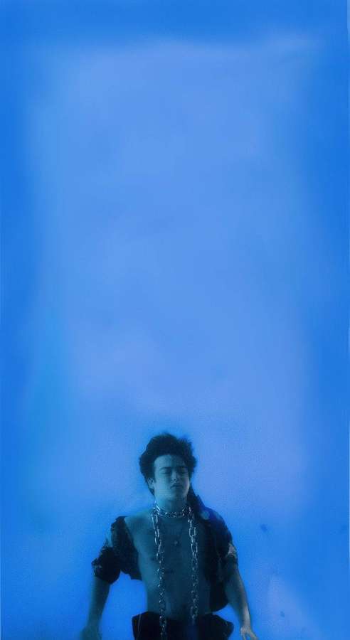 A person wearing chains submerged in blue water with a hazy atmosphere. — Joji Background