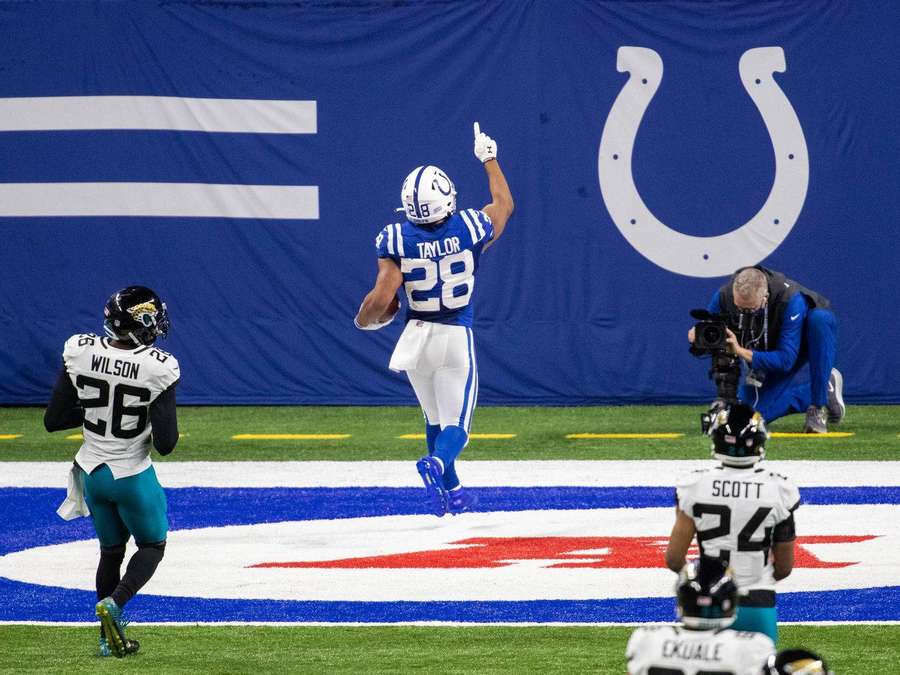 Football player celebrates touchdown with finger pointing skyward. — Jonathan Taylor Background