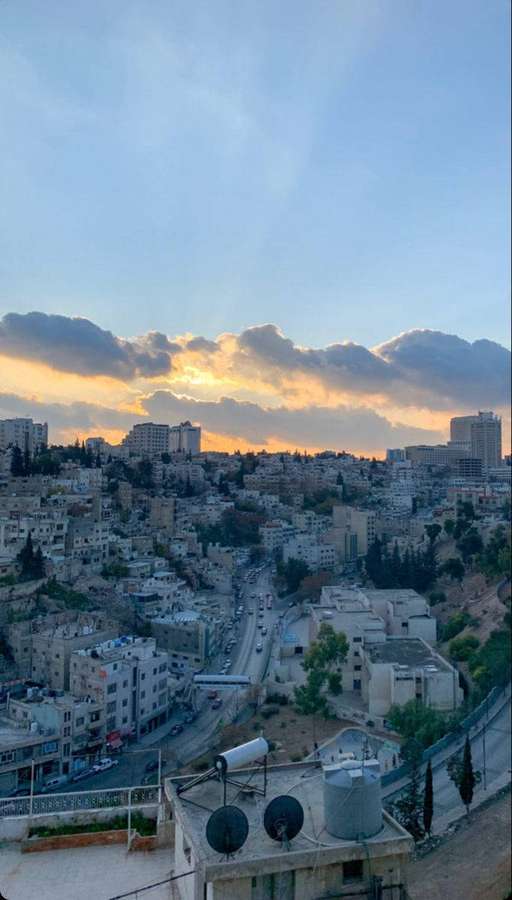 Paisagem urbana ao pôr do sol com nuvens douradas e estradas sinuosas em uma encosta. — Jordânia Papéis de Parede