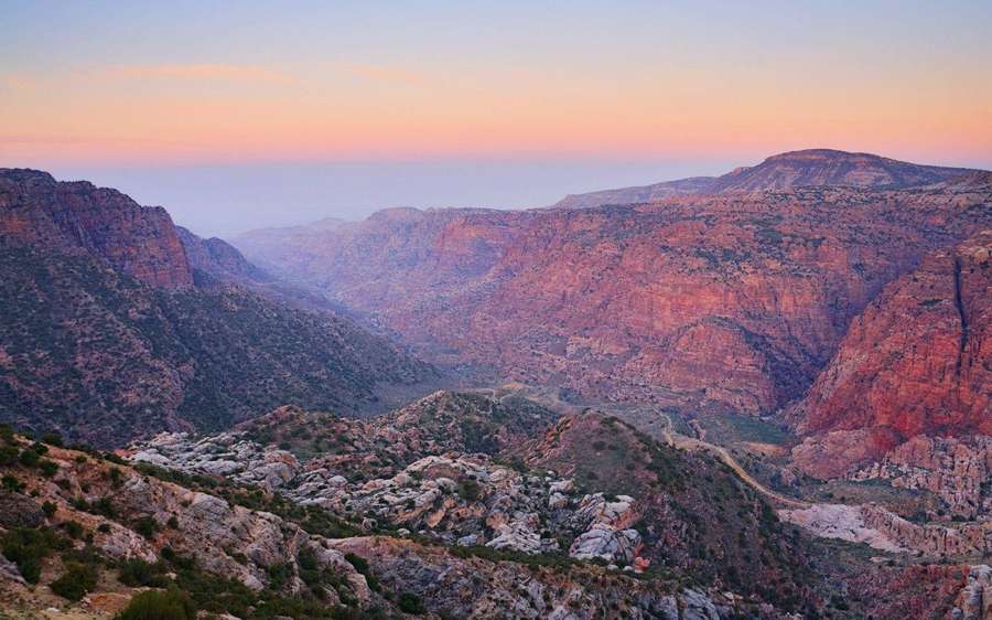 Sonnenuntergang über einer riesigen roten Felsenschlucht mit geschichteten Klippen und spärlicher Vegetation. — Jordanien Wallpaper