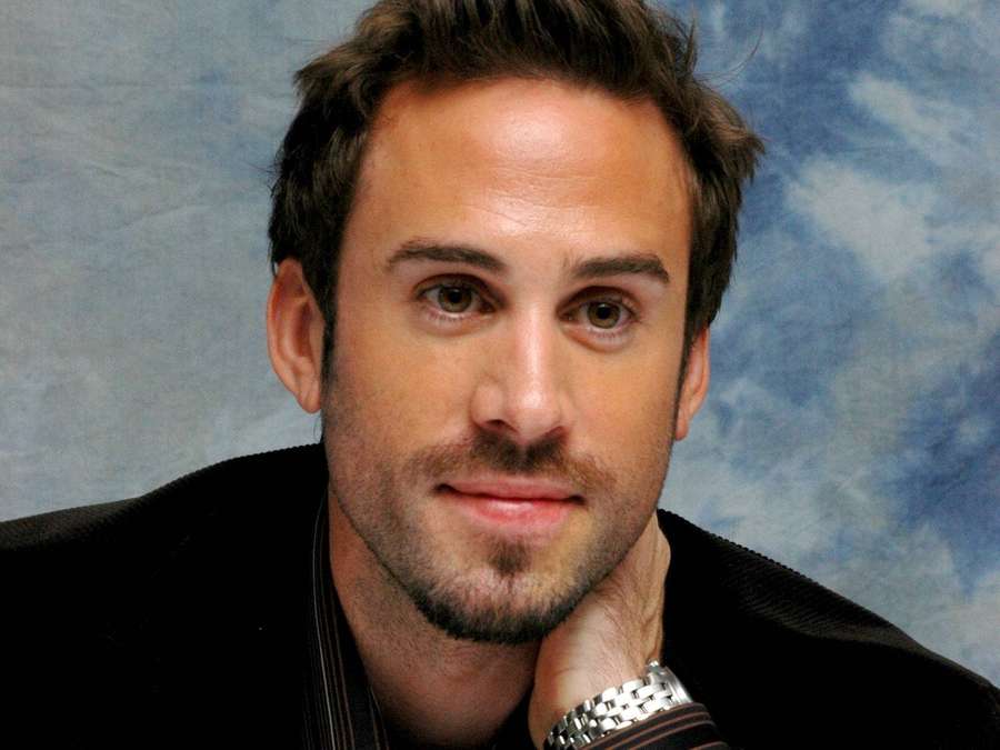 Man in black jacket with silver watch resting his chin on his hand. — Joseph Fiennes Wallpaper