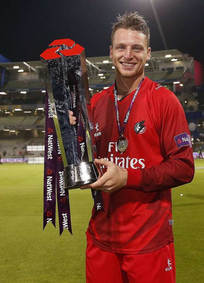 Jogador de rugby de uniforme vermelho segurando um troféu prateado à noite em um campo de estádio. — Josh Buttler Papéis de Parede