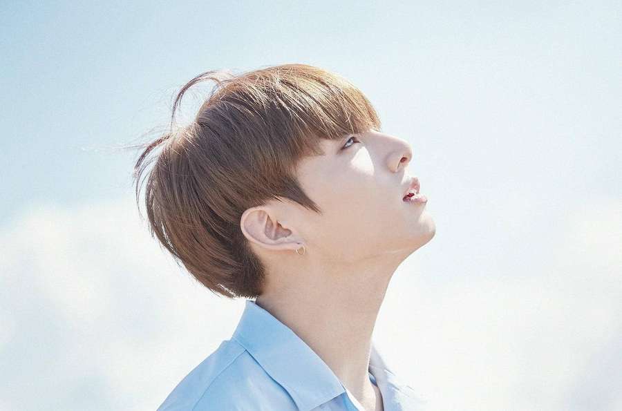 Junger Mann in blauem Hemd blickt zu hellem Himmel mit Wolken auf — Jungkook Wallpaper