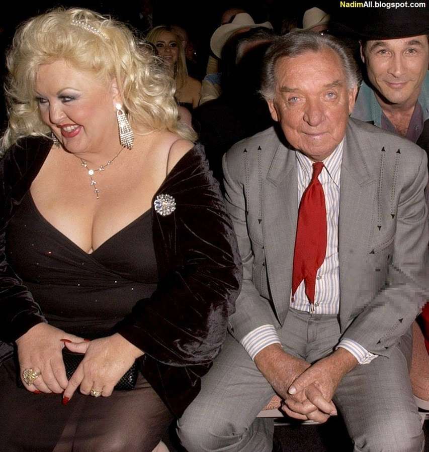 Una mujer con un vestido de terciopelo negro y un hombre con un traje gris y una corbata roja sentados juntos en un evento. — Juntos Fondos de pantalla