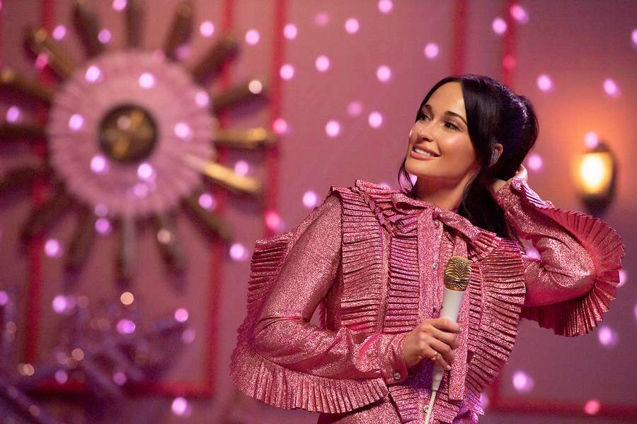 Frau in pinker Glitzerjacke singt auf einer beleuchteten Bühne mit dekorativer Sonne im Hintergrund. — Kacey Musgraves Wallpaper