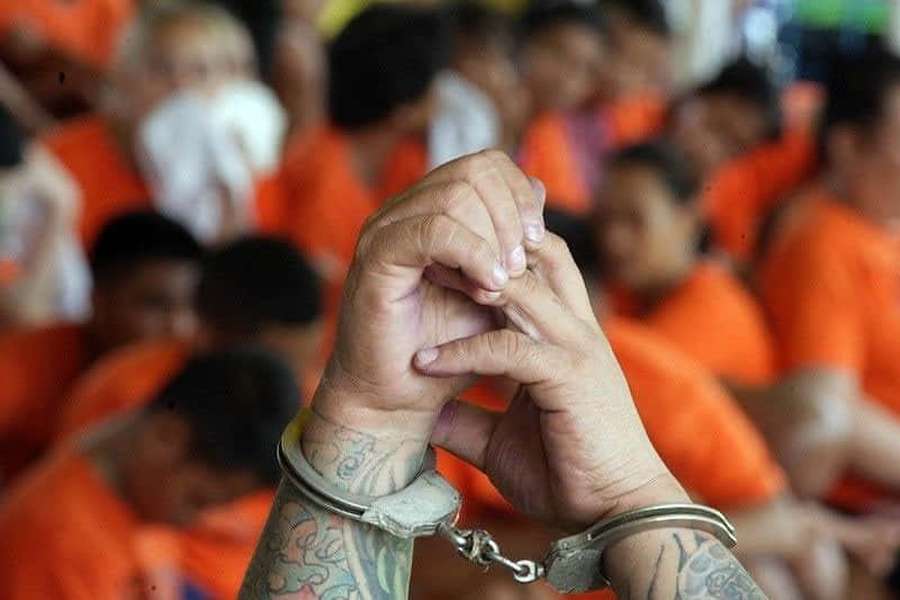 Tatuoidut kädet käsiraudoissa, takana sumeita vankeja oransseissa univormuissa. — Kammottava Taustakuvat