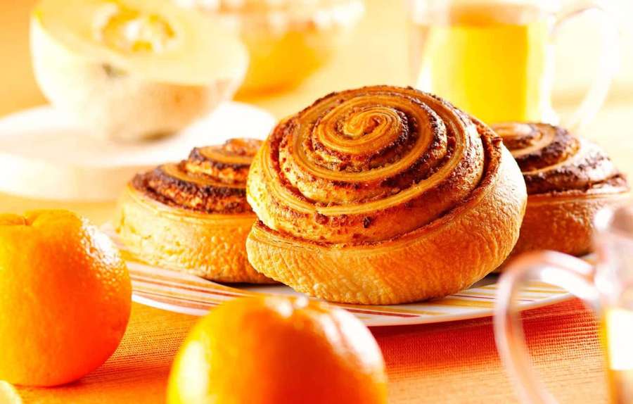 Juuri leivotut kanelipullat appelsiinien ja appelsiinimehun kanssa aamiaispöydällä. — Kanelipulla Taustakuvat