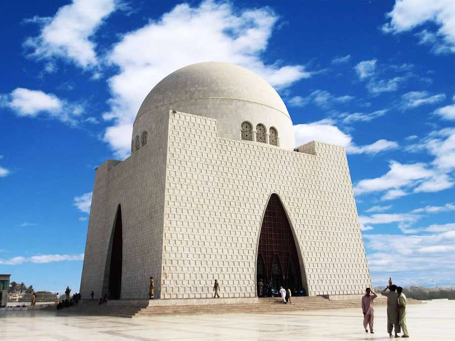 White domed mausoleum with people visiting under a bright blue sky. — Karachi Wallpaper