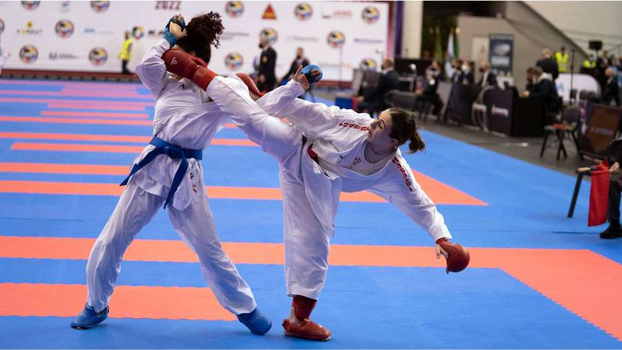 Dos luchadoras de taekwondo en uniformes blancos compiten en una colchoneta azul y naranja. — Karate Fondos de pantalla