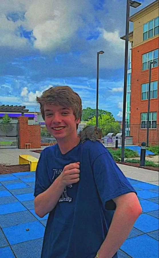 A young man smiles while a squirrel sits on his shoulder in a blue-tiled courtyard. — Karl Background