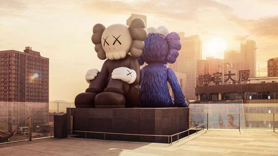 Two large KAWS sculptures embracing on a rooftop at sunset in a city. — Kaws Bff Wallpaper