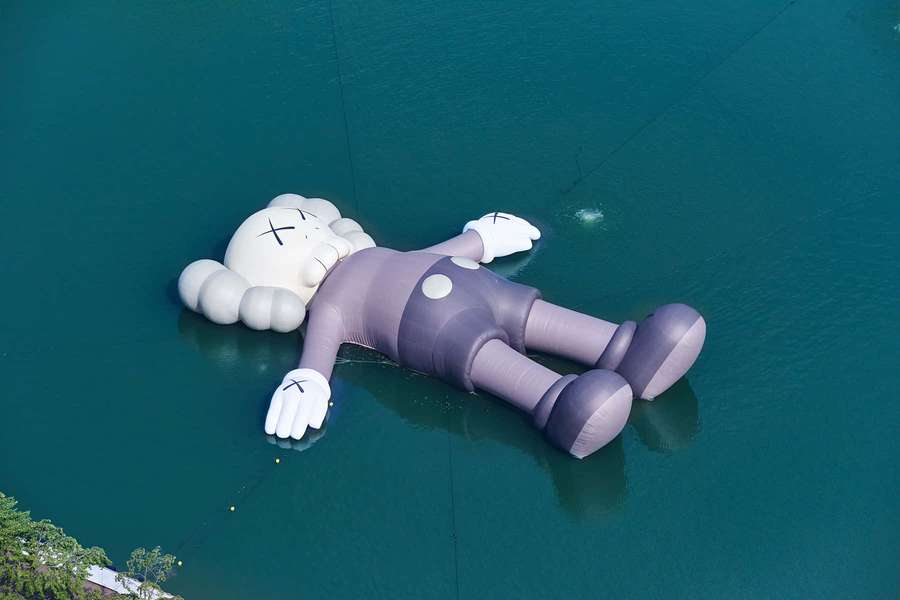 Large inflatable KAWS sculpture floating on calm turquoise water. — Kaws Holiday Wallpaper