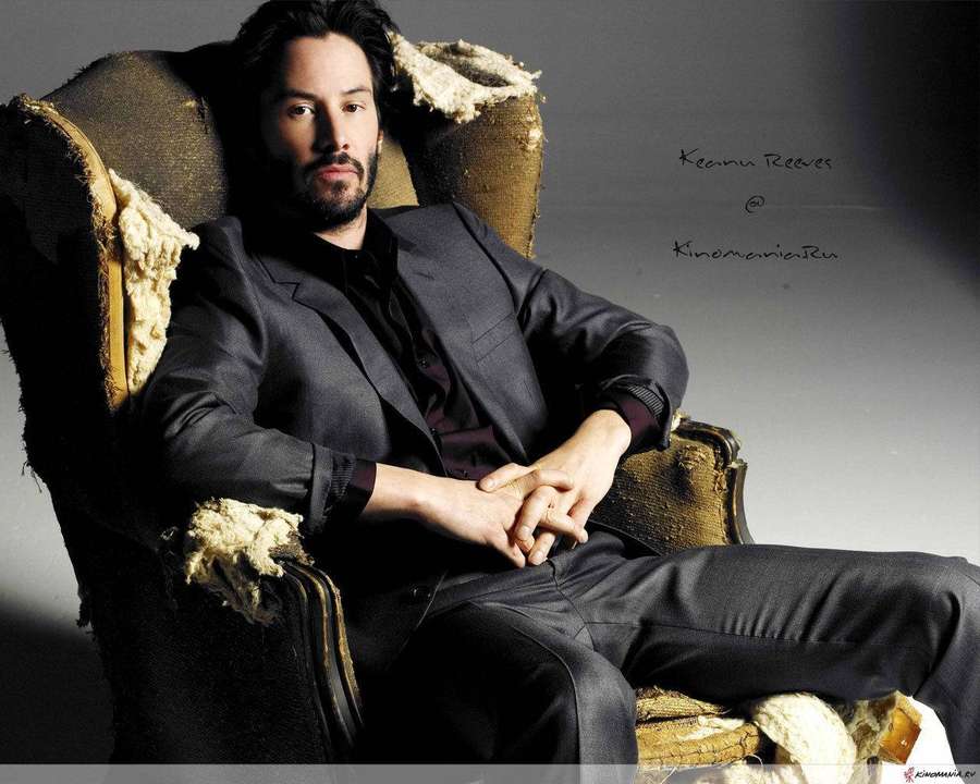 Man in dark suit seated in worn armchair with torn fabric — Keanu Wallpaper