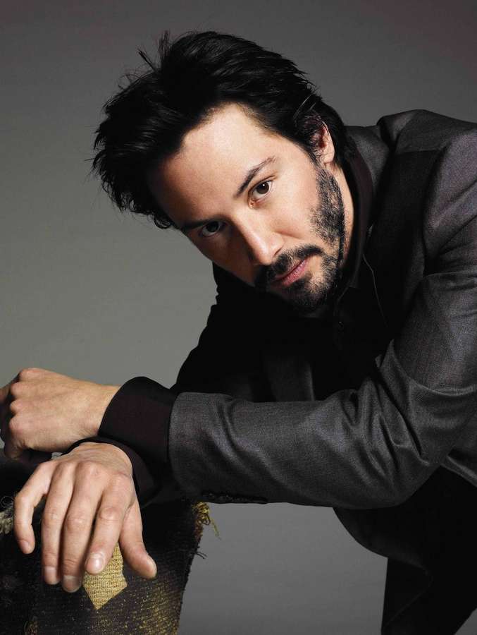 Man in dark suit leaning forward with intense gaze in studio portrait. — Keanu Reeves Wallpaper