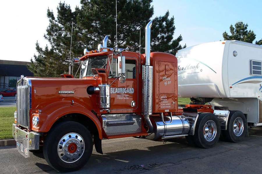 Orange Kenworth semi truck towing a white RV parked on asphalt near trees. — Kenworth C500 Wallpaper