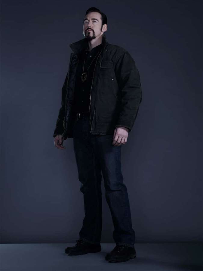 A man in dark clothing poses in a studio with dramatic lighting. — Kevin Durand Picture