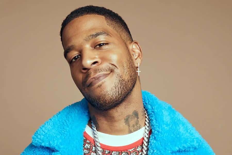 Mies, jolla on tatuointeja ja ristikorvakoru, yllään sininen pörröinen takki — Kid cudi Taustakuvat