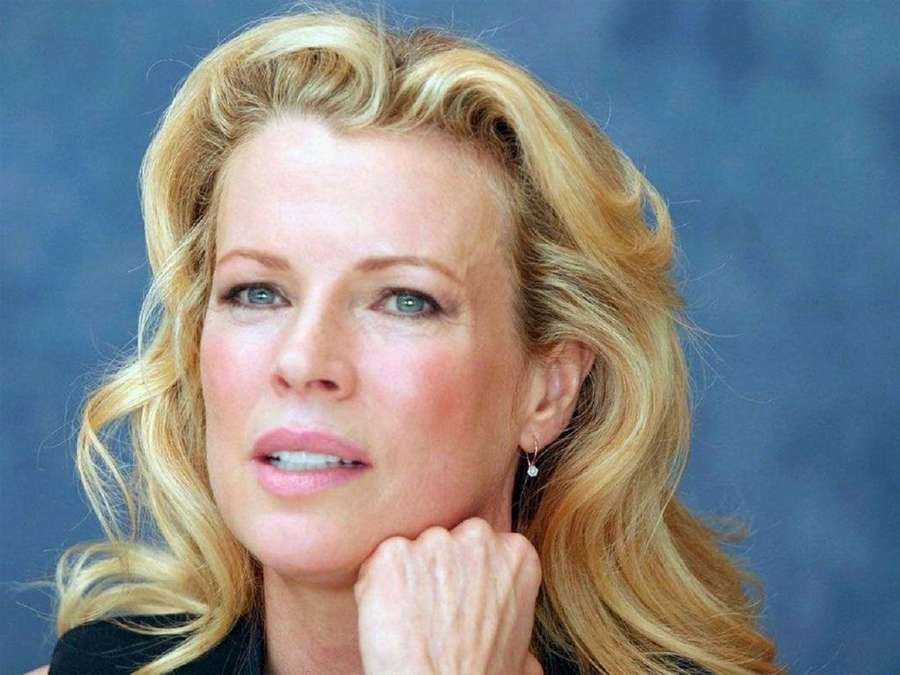 Blonde Frau mit blauen Augen, die ihr Kinn auf ihre Hand stützt, vor blauem Hintergrund. — Kim basinger Bilder