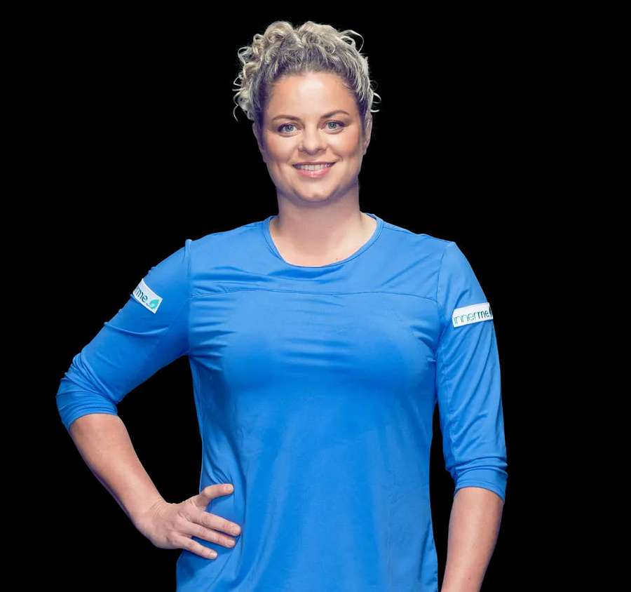 Woman in blue athletic shirt smiling with hand on hip against black background — Kim Clijsters Wallpaper