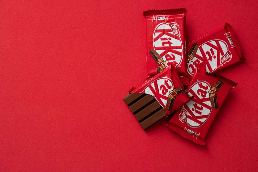 Five KitKat chocolate bars with one unwrapped on a red background. — Kit Kat Picture