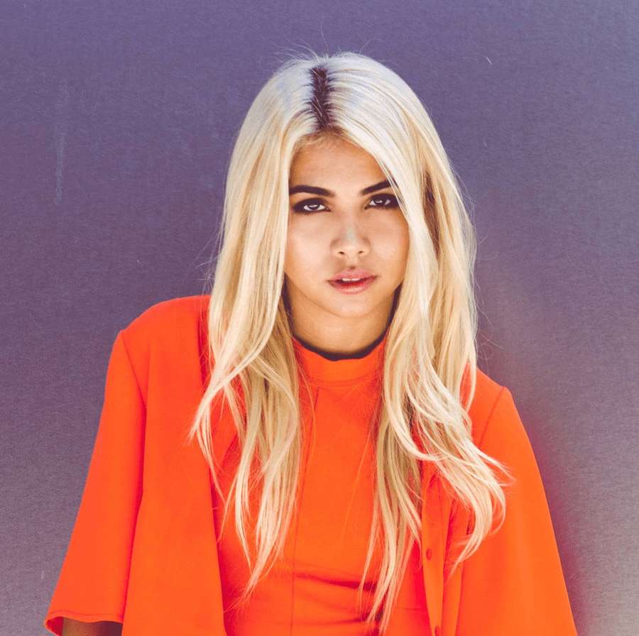 A woman with blonde hair and orange clothing poses against a purple background. — Kiyoko Background