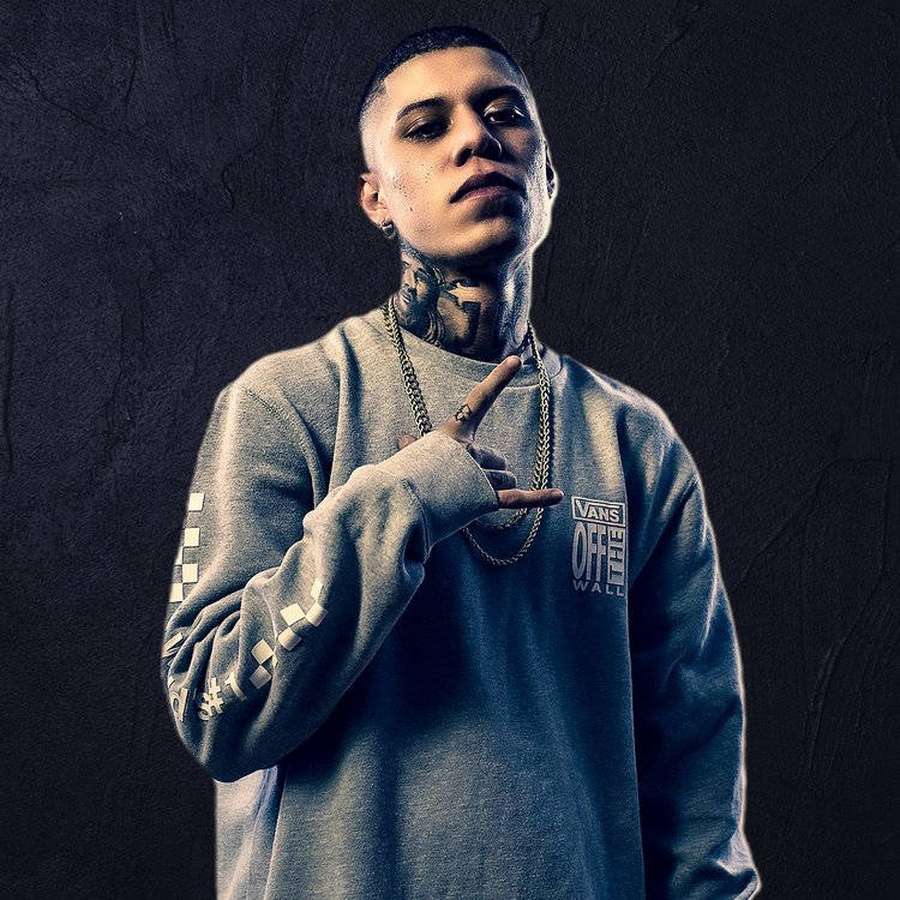 Tätowierter Mann in grauem Sweatshirt macht Handgeste vor dunkler Wand. — Klan Bilder