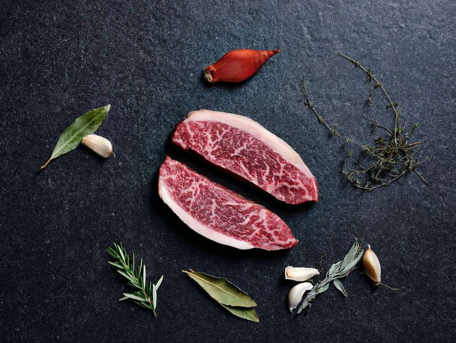Kaksi raakaa naudanlihapihviä yrteillä ja valkosipulilla tummalla liuskekivitaustalla. — Kobe Beef Taustakuvat