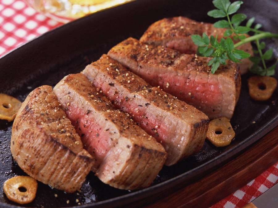 Aufgeschnittenes medium-rare Steak mit Kräutern und Oliven auf einem schwarzen Teller. — Kobe Beef Bilder