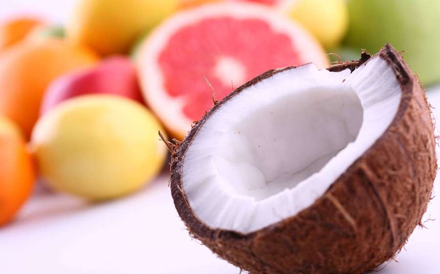 Eine aufgebrochene Kokosnuss mit weißem Fruchtfleisch, umgeben von bunten Zitrusfrüchten. — Kokosnuss Wallpaper