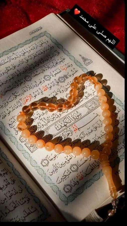 Herzförmige Bernstein-Gebetsperlen auf einem offenen Koran mit arabischem Text. — Koran bilder