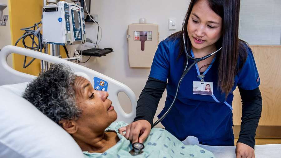 Krankenschwester überprüft den Herzschlag eines Patienten mit Stethoskop im Krankenhausbett — Krankenhausbett Wallpaper