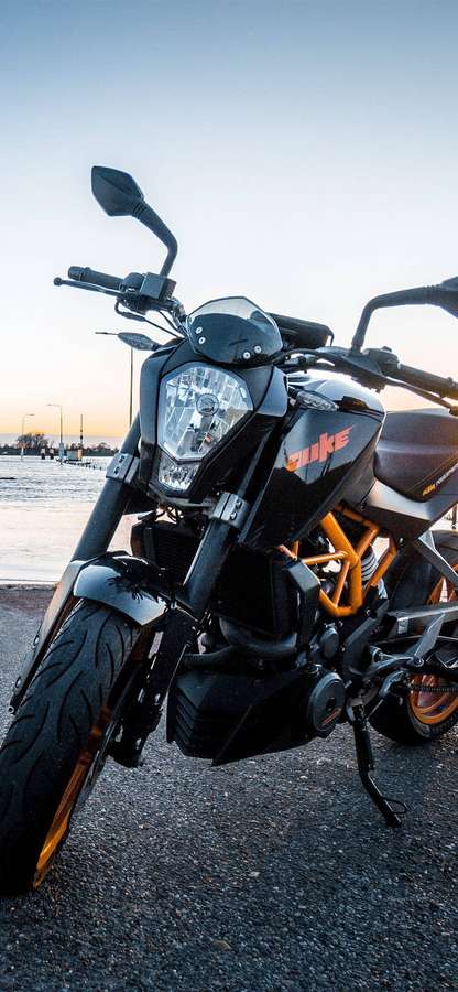 Sort KTM Duke motorcykel med orange detaljer parkeret nær vand ved solnedgang. — Ktm iPhone Wallpapers