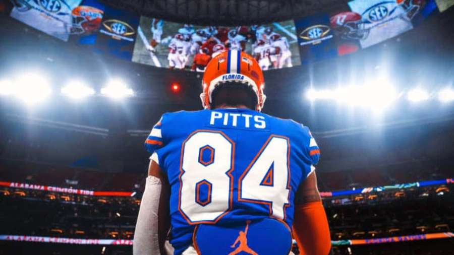 Pemain sepak bola Amerika nomor 84 dengan jersey biru berdiri di lapangan di bawah lampu stadion. — Kyle Pitts Wallpaper