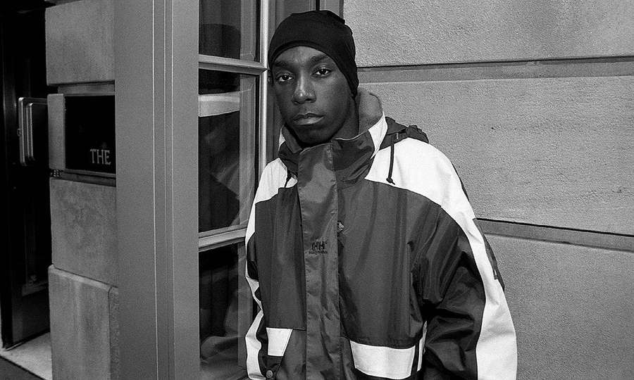 Jonge man in streetwear-jack en muts bij de ingang van een gebouw — L Achtergronden